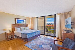 Habitación de hotel con cama, televisión, silla, balcón con vistas y ventana con cortinas.