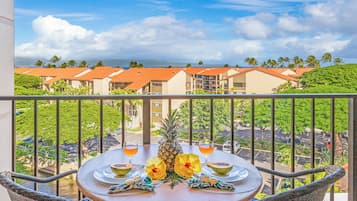 Ein Balkon mit Tisch für zwei Personen, mit Blick auf eine Wohngegend mit roten Dächern und Palmen.