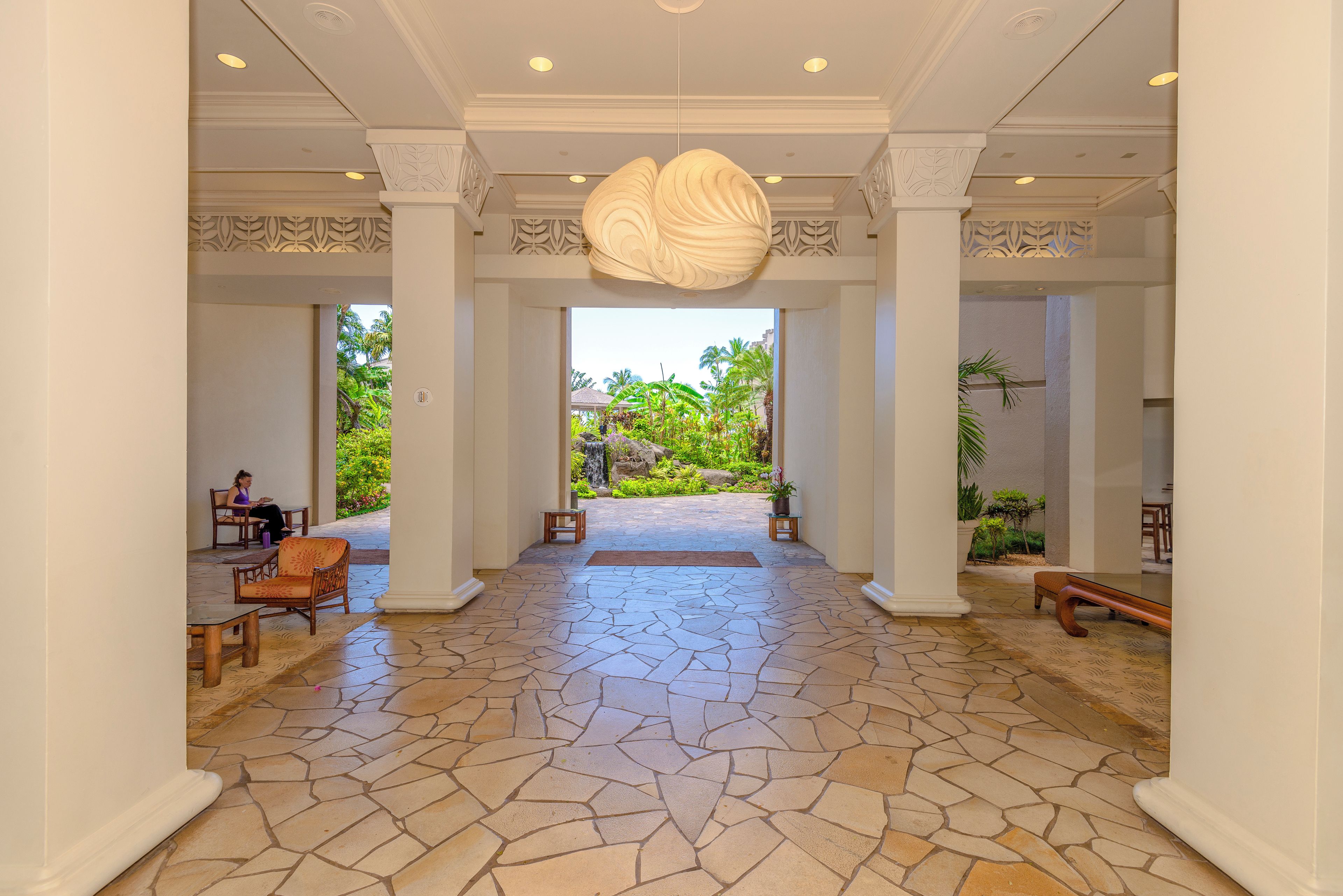 A spacious lobby with a stone floor, a large decorative light fixture, and a view of a tropical garden.