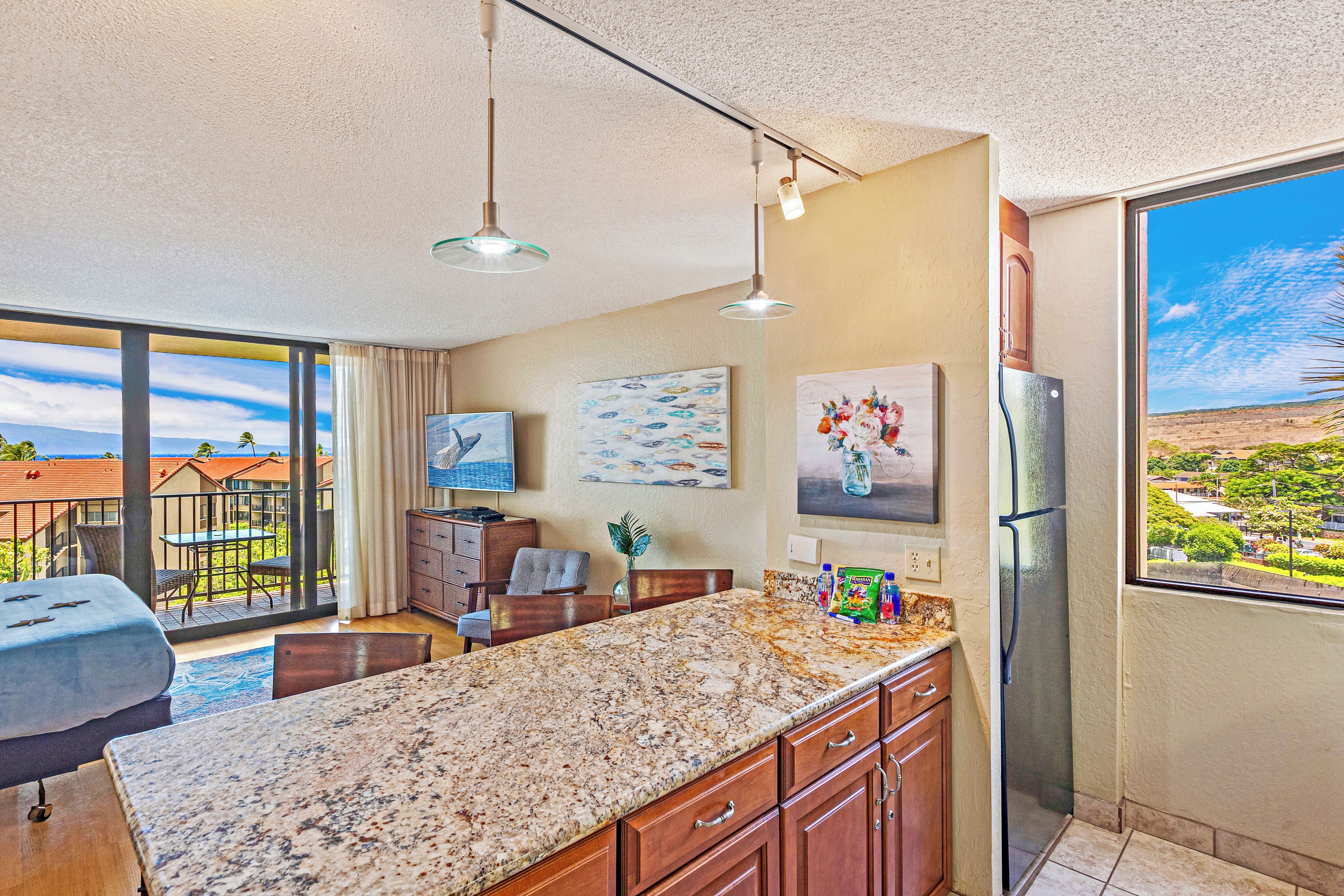 A modern kitchen with a large island, pendant lights, and a view of the ocean.