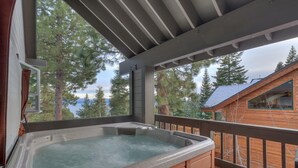 Un bain à remous sur un balcon avec vue sur les arbres et un chalet.