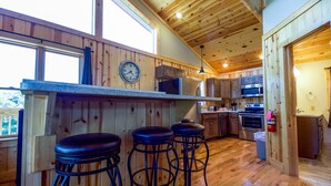 Una cucina con pareti in legno, una sveglia, un angolo bar con sgabelli ed elettrodomestici moderni.