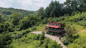 Un edificio moderno a due piani con tetto rosso, immerso nel verde e circondato da dolci colline.