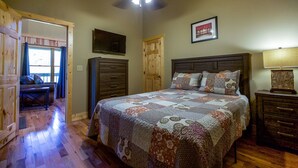 Una camera da letto con soffitto in legno, un letto con copripiumino a fantasia, un comodino, una cassettiera e una porta che dà su un'altra stanza.