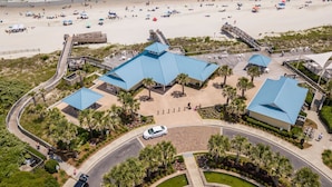 A coastal hotel with a blue-roofed main building, a boardwalk, and a beach view. - Heron Marsh 86 in Litchfield By the Sea, steps away from the pool and beach (Pawleys Island)