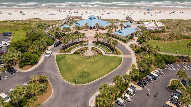 An aerial view of a coastal resort with a central building surrounded by a landscaped area, a parking lot, and a beach in the background. - Heron Marsh 86 in Litchfield By the Sea, steps away from the pool and beach (Pawleys Island)