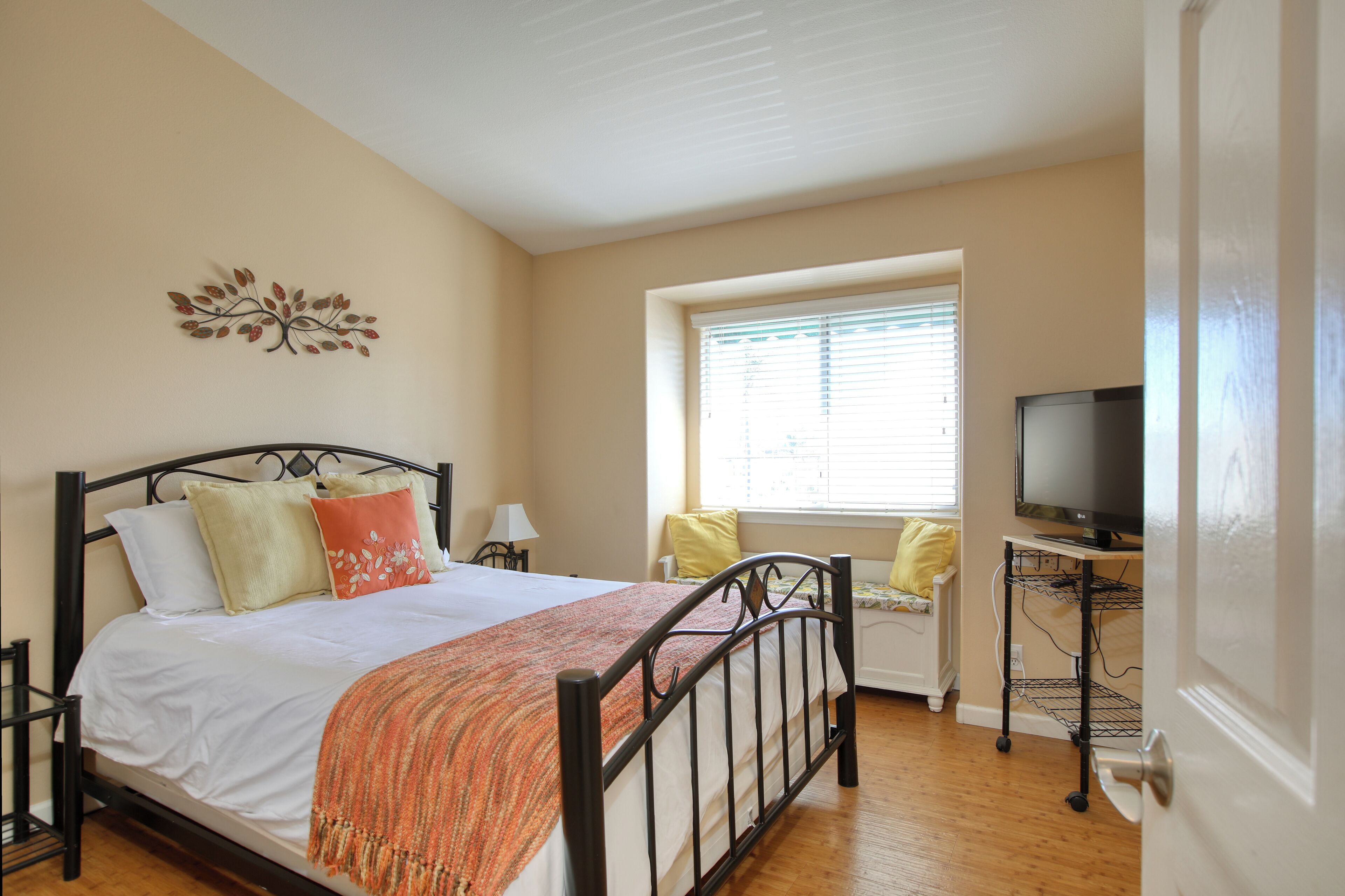 A bedroom with a bed, a television on a stand, a window with blinds, and a wall decoration.
