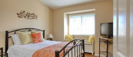 A bedroom with a bed, a television on a stand, a window with blinds, and a wall decoration.
