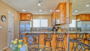Una cocina con armarios de madera, electrodomésticos de acero inoxidable, una isla de cristal con taburetes y una puerta con espejo.