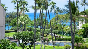 Un jardin luxuriant, avec des palmiers, un étang et une vue sur l’océan.
