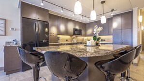 Une cuisine moderne avec des meubles de couleur sombre, des appareils en acier inoxydable et un îlot central doté de tabourets de bar.