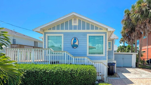 A single-story building with a blue exterior, a white porch, and a small front yard with a hedge and grass. - 213 Ohio Cozy Cottage Just Short Walk to Beach (Fort Myers Beach)