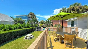 A wooden deck with outdoor furniture, a pool, and a clear blue sky. - 213 Ohio Cozy Cottage Just Short Walk to Beach (Fort Myers Beach)