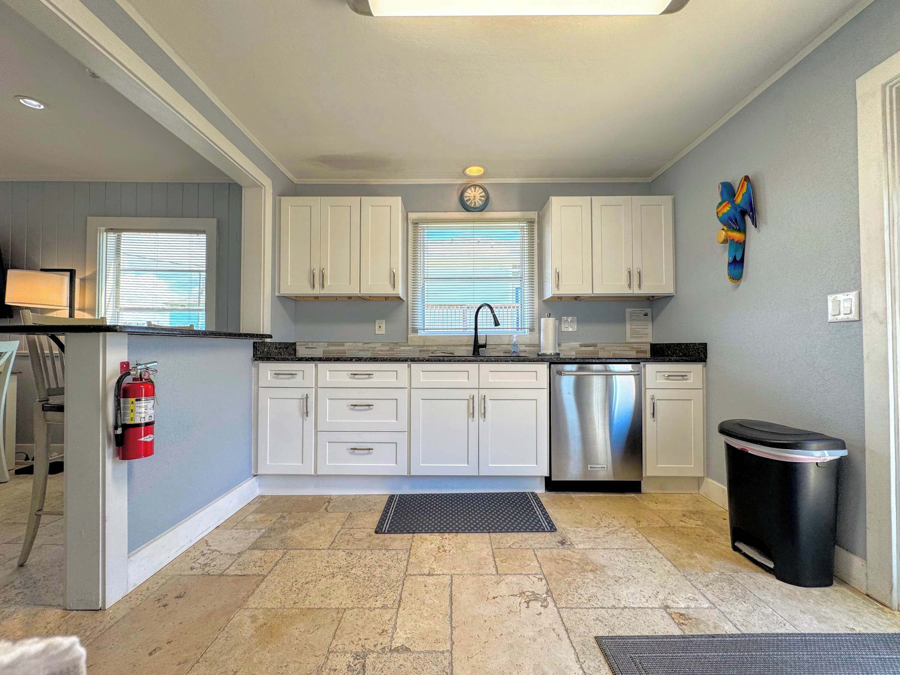 A kitchen with white cabinets, a stainless steel dishwasher, and a black trash can.