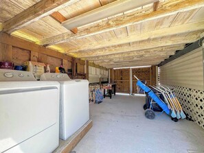 A laundry room with stacked laundry, a washing machine, and a cart with cleaning supplies. - 213 Ohio Cozy Cottage Just Short Walk to Beach (Fort Myers Beach)