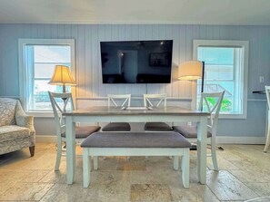 A dining area with a table, chairs, and a television mounted on the wall. - 213 Ohio Cozy Cottage Just Short Walk to Beach (Fort Myers Beach)