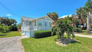 A single-story house with a covered porch, surrounded by well-maintained grass and palm trees. - 213 Ohio Cozy Cottage Just Short Walk to Beach (Fort Myers Beach)