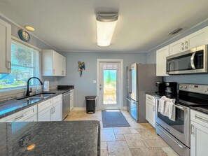 A modern kitchen with white cabinets, a stainless steel refrigerator, a microwave, and a coffee maker. - 213 Ohio Cozy Cottage Just Short Walk to Beach (Fort Myers Beach)