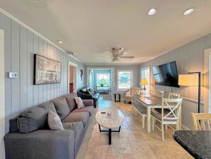 A living room with a sofa, a coffee table, a TV, and a dining area with chairs and a table. - 213 Ohio Cozy Cottage Just Short Walk to Beach (Fort Myers Beach)
