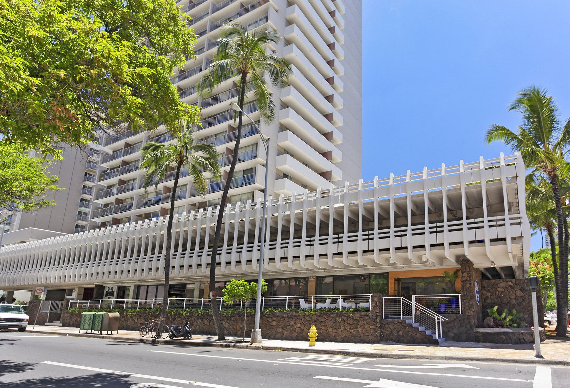 A modern hotel with a multi-story structure, a covered pedestrian walkway, and a stone facade.