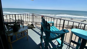 Un balcone con vista sulla spiaggia, dotato di un tavolo, sedie e una pianta in vaso.