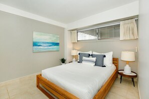 A bedroom with a wooden bed, two bedside tables with lamps, a window with curtains, and a painting on the wall.