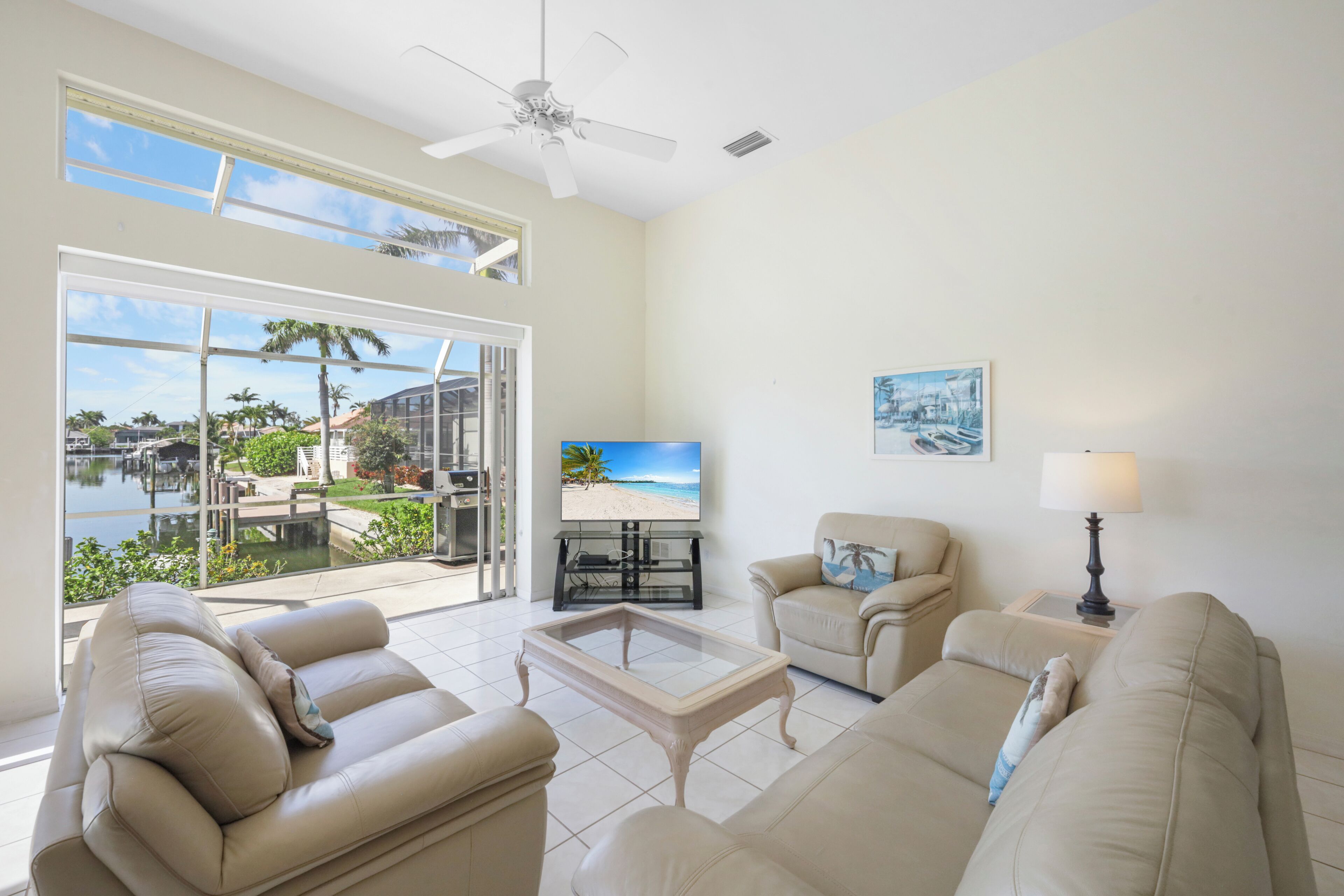 A spacious living room with a large window overlooking a water view, a ceiling fan, and a television on a stand.
