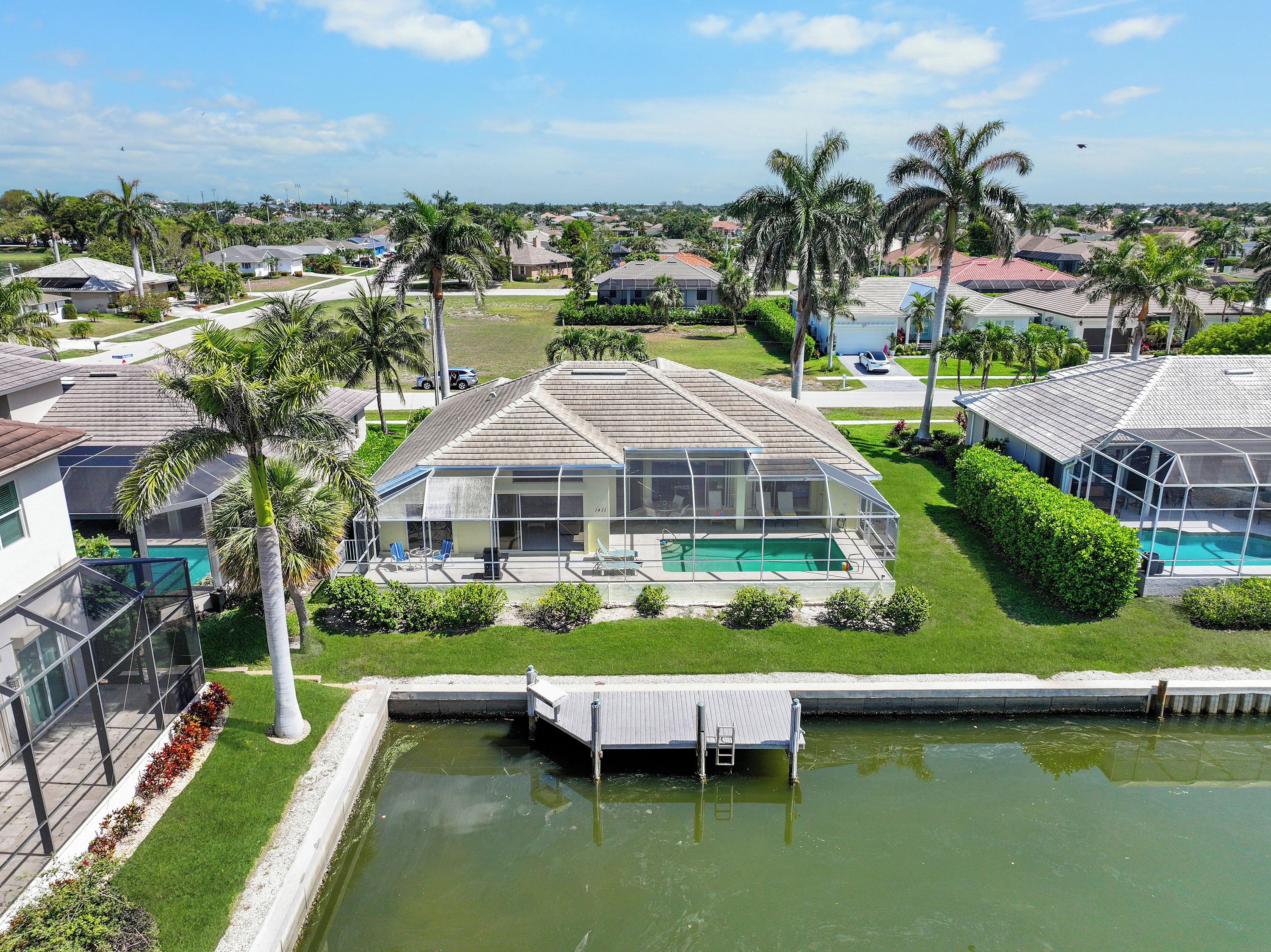 A house with a large glass-enclosed pool area, surrounded by palm trees and a well-maintained lawn.