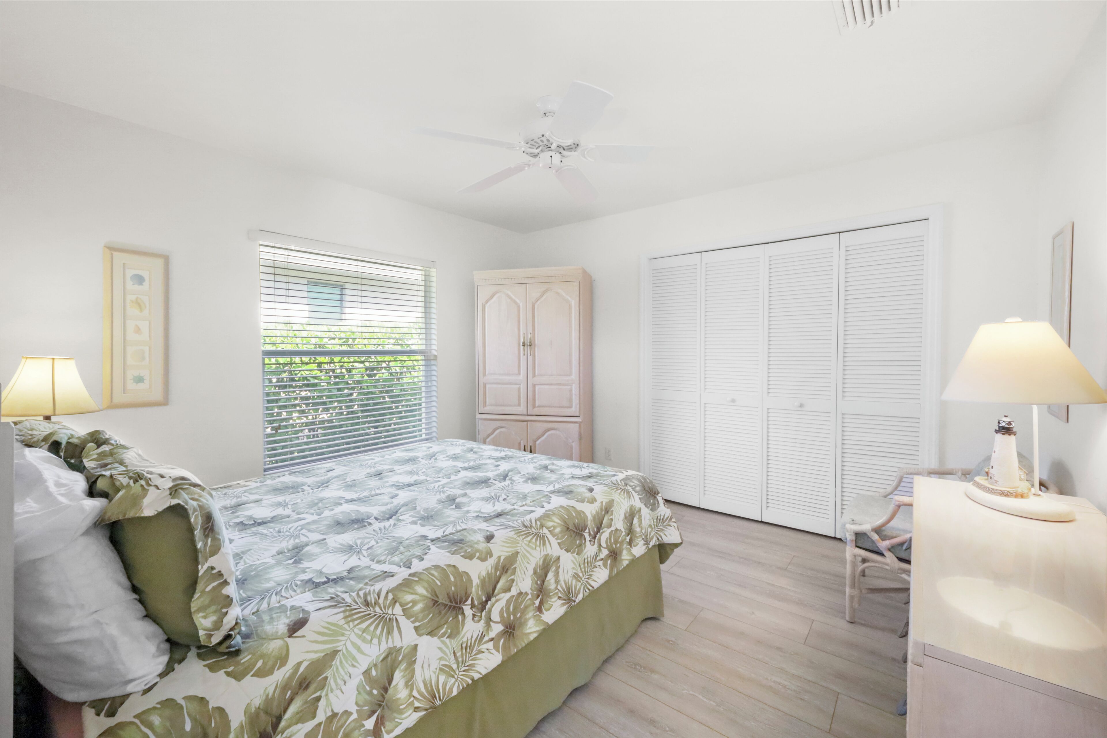 Une chambre à coucher comprenant un lit, une armoire, un bureau avec une lampe et un ventilateur de plafond.