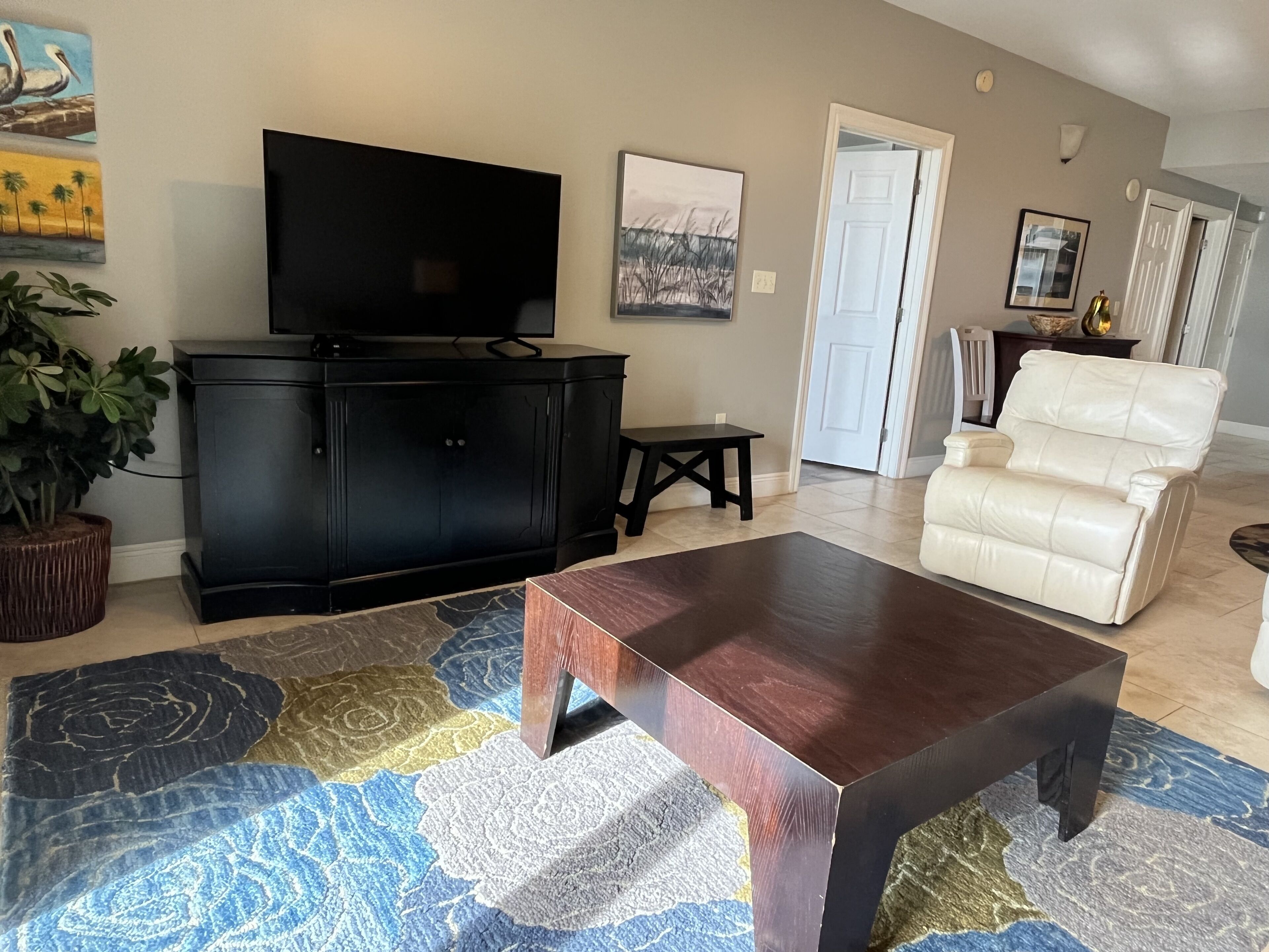 A living room with a black entertainment unit, a white leather sofa, a wooden coffee table, and a patterned rug.