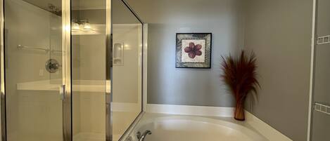 A bathroom with a glass-enclosed shower, a freestanding bathtub, and a framed botanical print on the wall.