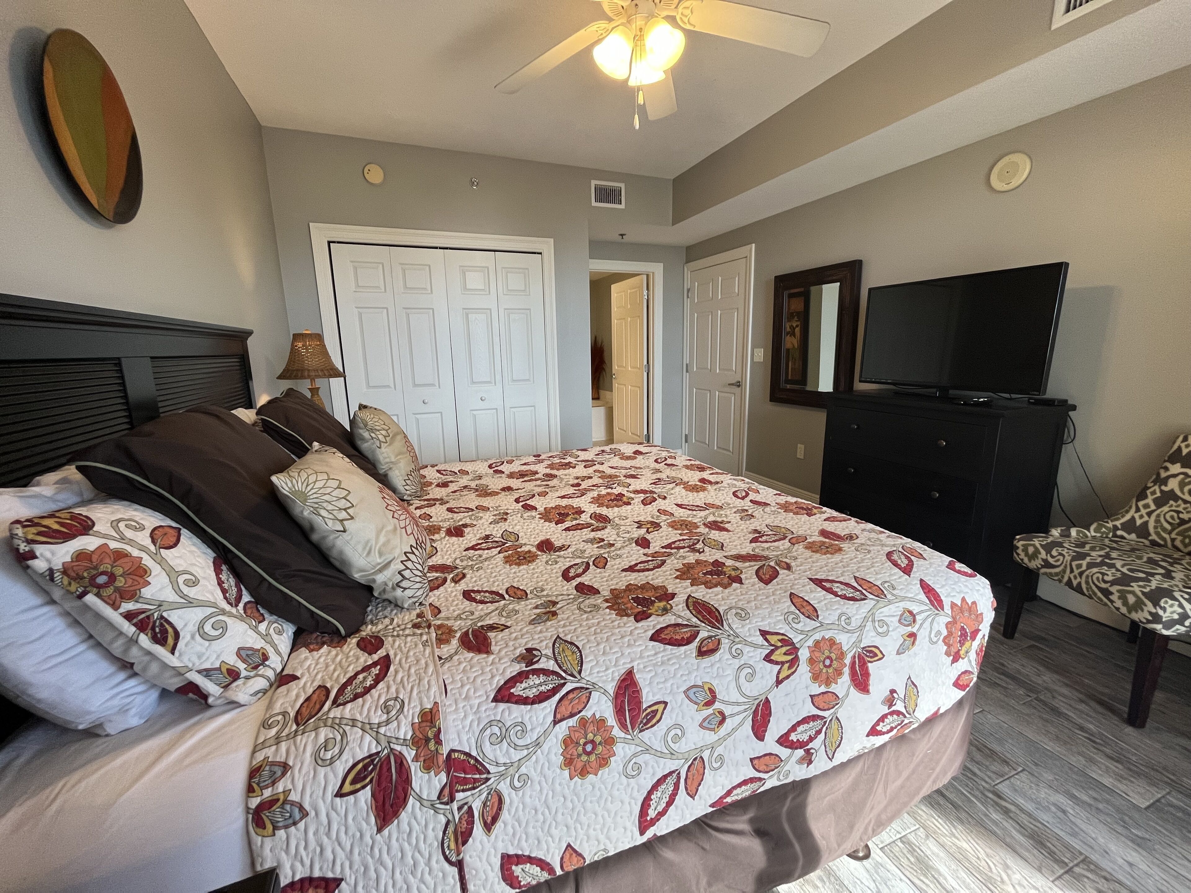 A bedroom with a large bed, a ceiling fan, a TV, and a dresser.