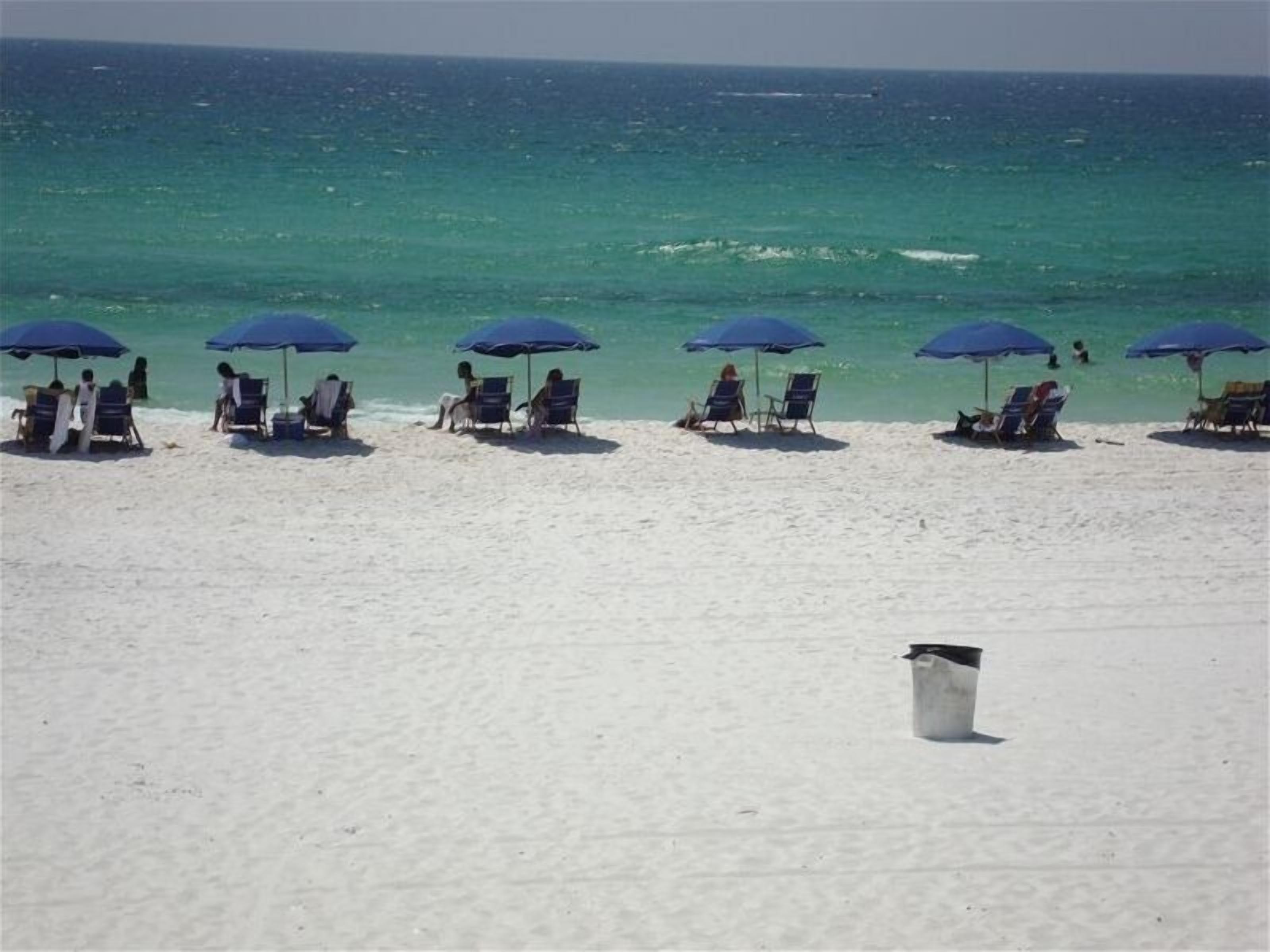 A beach with rows of beach chairs and umbrellas, a white trash bin, and the ocean in the background.