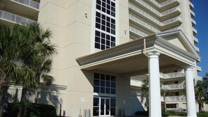 Un hotel de varios pisos con una entrada destacada, grandes ventanales y un corredor cubierto sostenido por columnas.