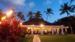 An outdoor restaurant with a covered seating area, palm trees, and a pathway leading to the entrance. - Private luxury home with high ceilings and room for 6 (Kamuela)