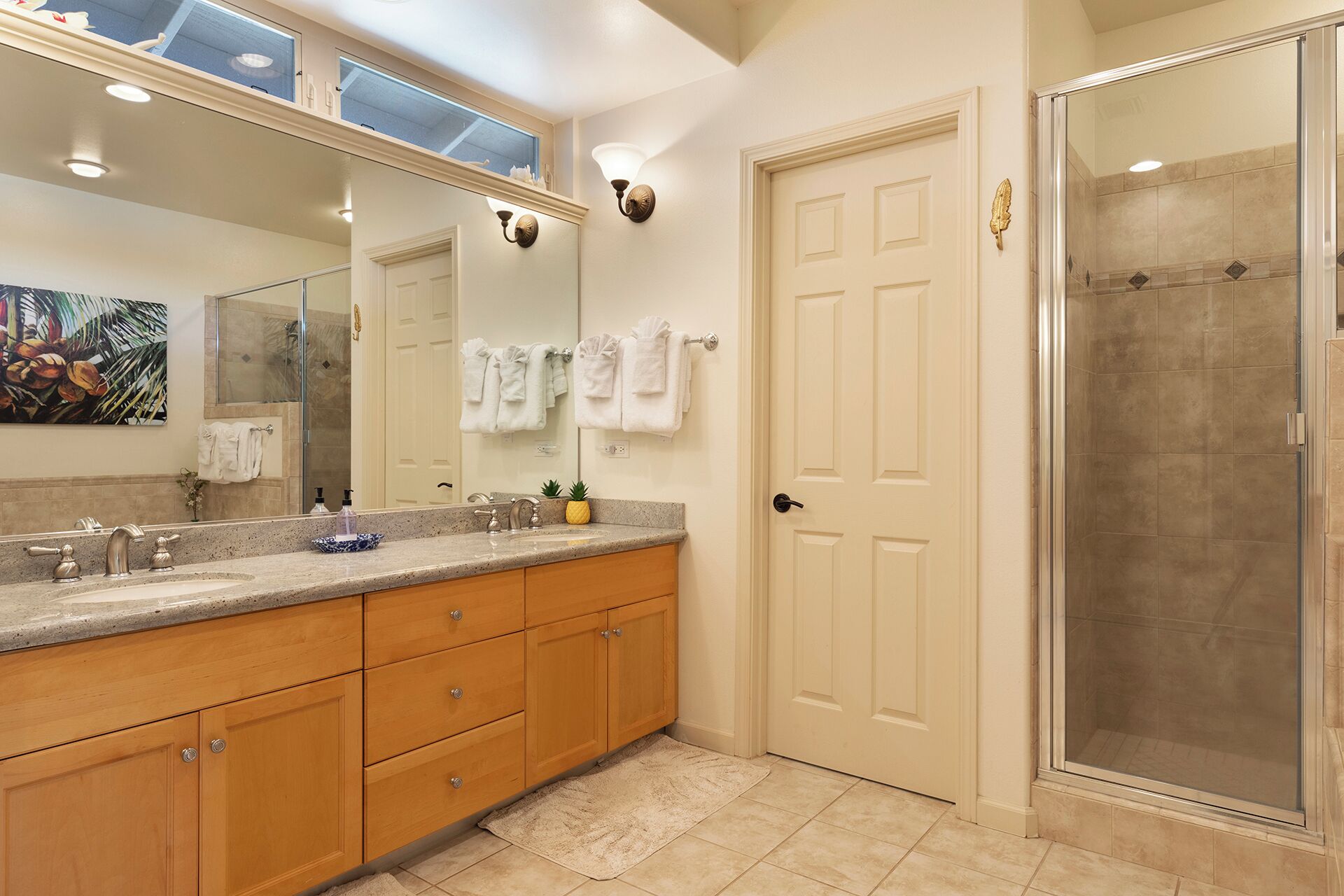 A bathroom with a double vanity, a glass shower enclosure, and a large mirror with a decorative wall piece.