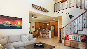 A spacious living area with a sofa, coffee table, and a kitchen in the background. - Private luxury home with high ceilings and room for 6 (Kamuela)