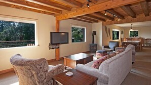Una sala de estar amplia con techo de madera, televisor, chimenea y comedor con mesa y sillas.