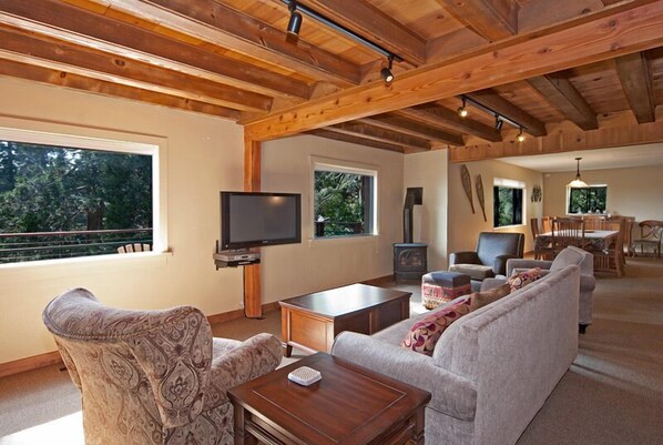 A spacious living room with a wooden ceiling, a television, a fireplace, and a dining area with a table and chairs.