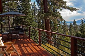 A wooden deck with outdoor furniture, a table, and chairs, overlooking a forest and a lake.