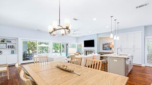 A spacious kitchen with a large island, wooden dining table, and modern pendant lighting.
