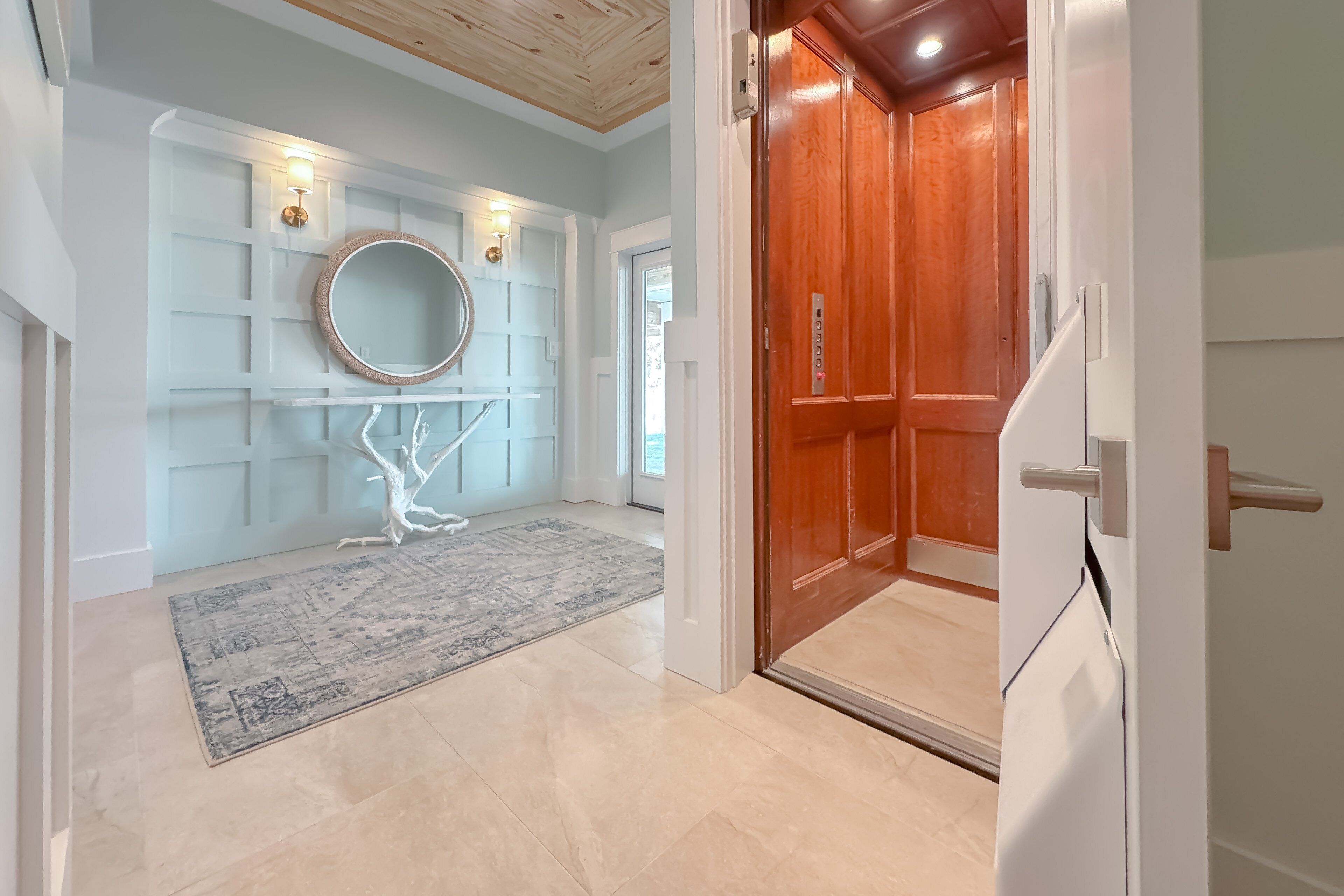 A modern interior with a wooden door, a white wall with a circular mirror, and a patterned rug.