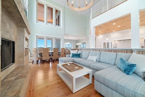 A spacious living area with a fireplace, a dining table with chairs, a large sofa, and a kitchen area with cabinets and a countertop.