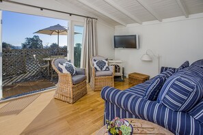 Une pièce spacieuse avec un grand canapé, deux fauteuils en osier, une petite table et un téléviseur fixé au mur.