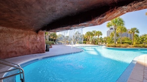 A swimming pool with a natural rock arch overhead, surrounded by palm trees and a clear sky. - Lockout Style ~ Gulf Views ~ Balcony ~ Resort Pool (Miramar Beach)