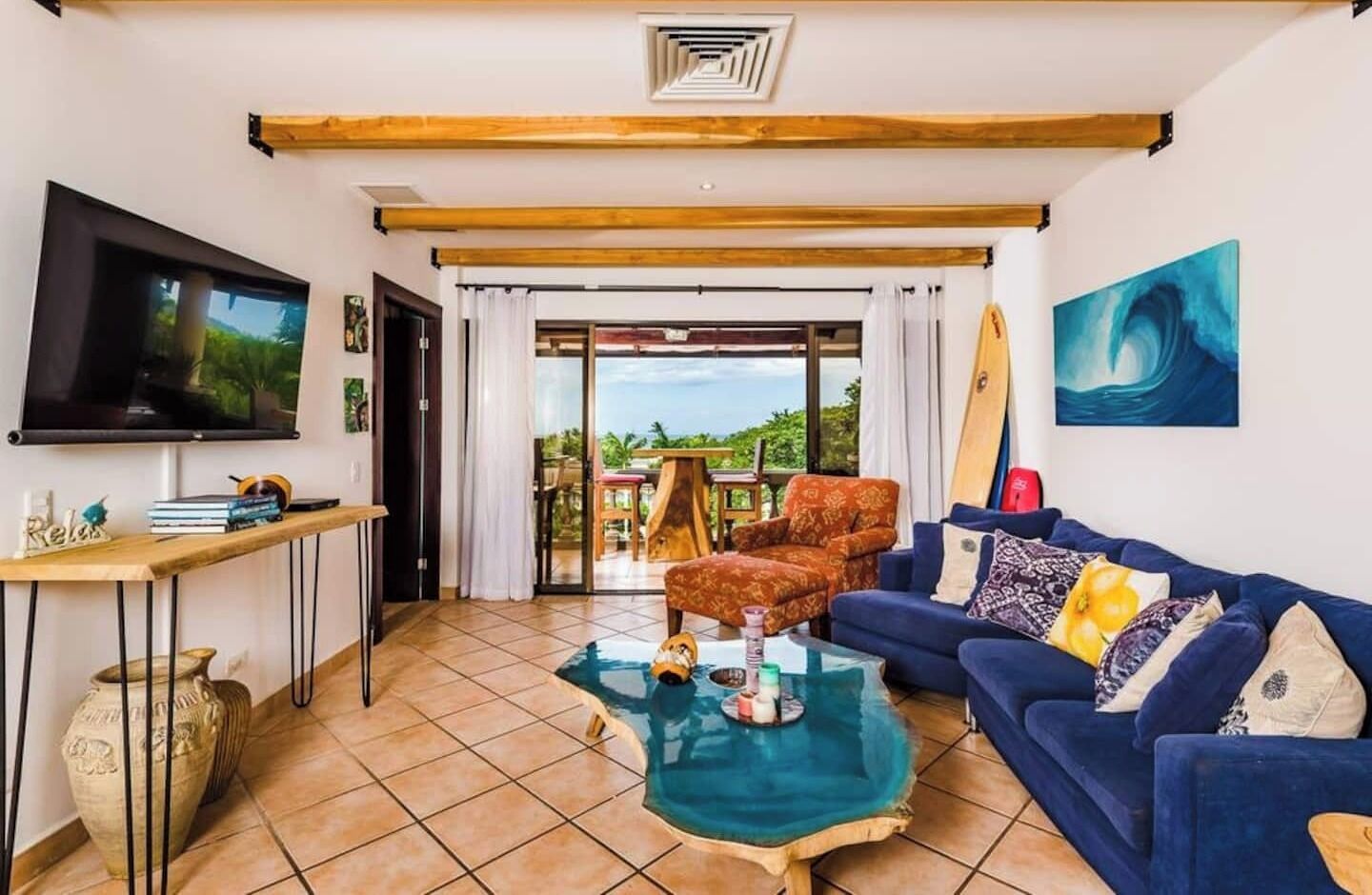 Una sala de estar con televisión, sofá, mesa de centro y vista al exterior.
