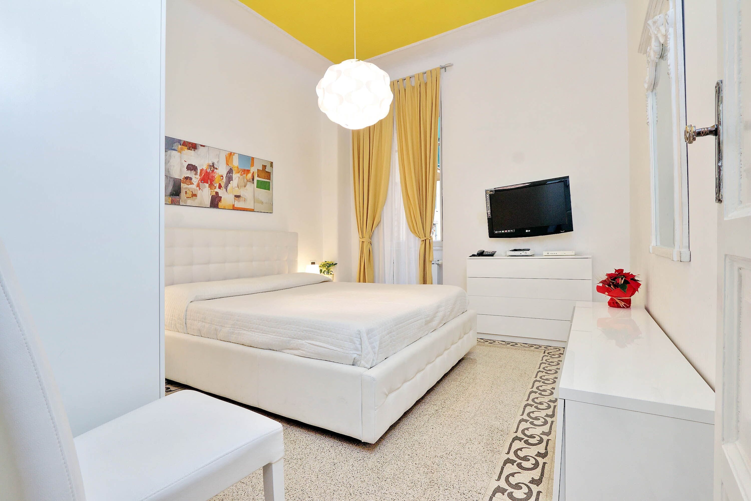 Un dormitorio moderno con cama, escritorio, televisor y un cuadro en la pared.