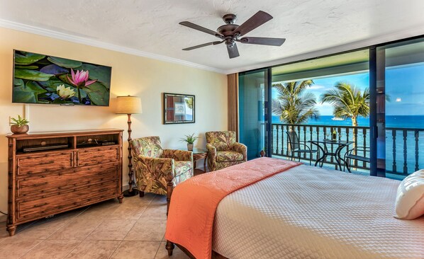 A bedroom with a bed, a ceiling fan, a TV, a dresser, and a view of the ocean.