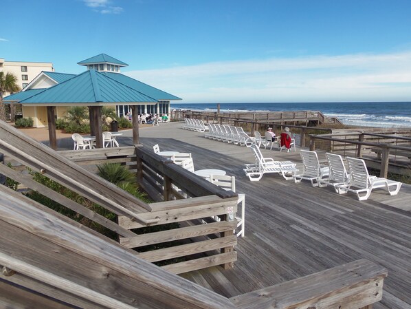 A wooden boardwalk with white lounge chairs and a gazebo overlooking the beach.