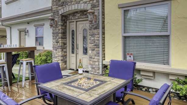 Une terrasse extérieure avec une table autour d’un foyer, deux chaises violettes et un mur en pierre.